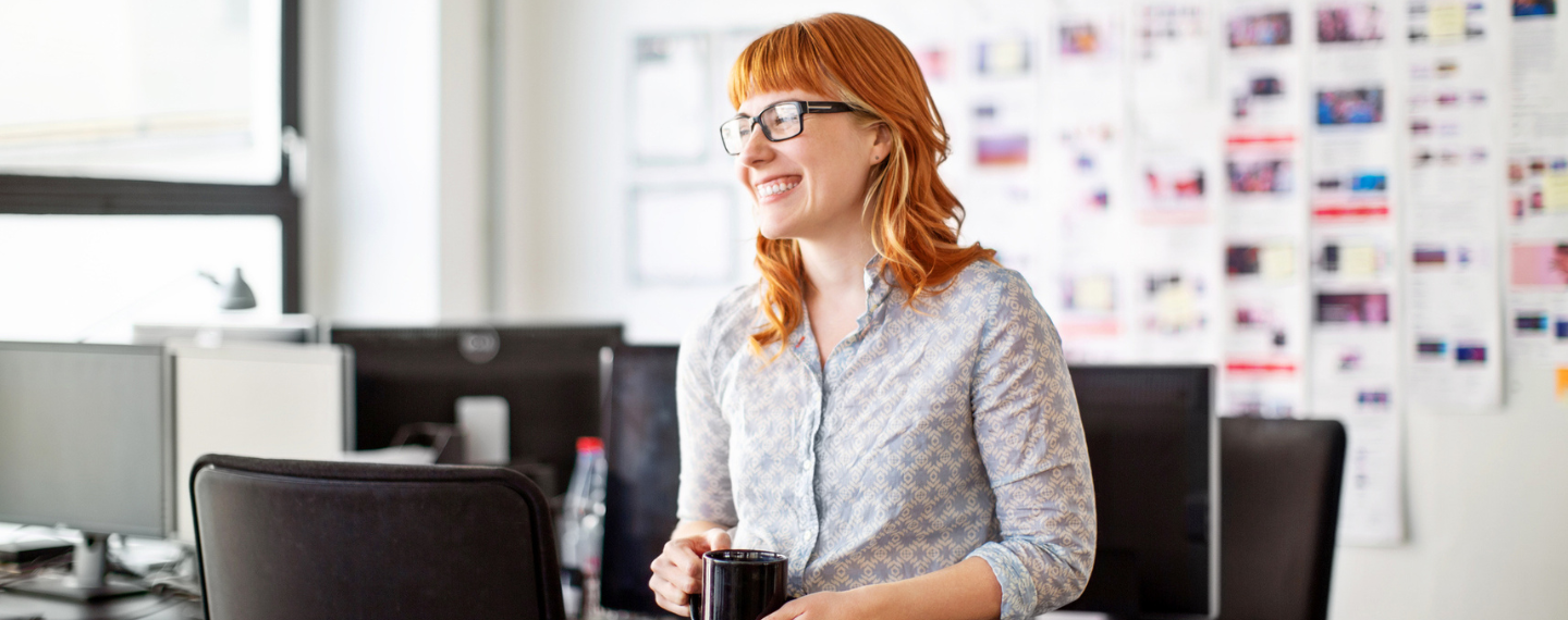 Smiling woman sits at desk and drinks coffee