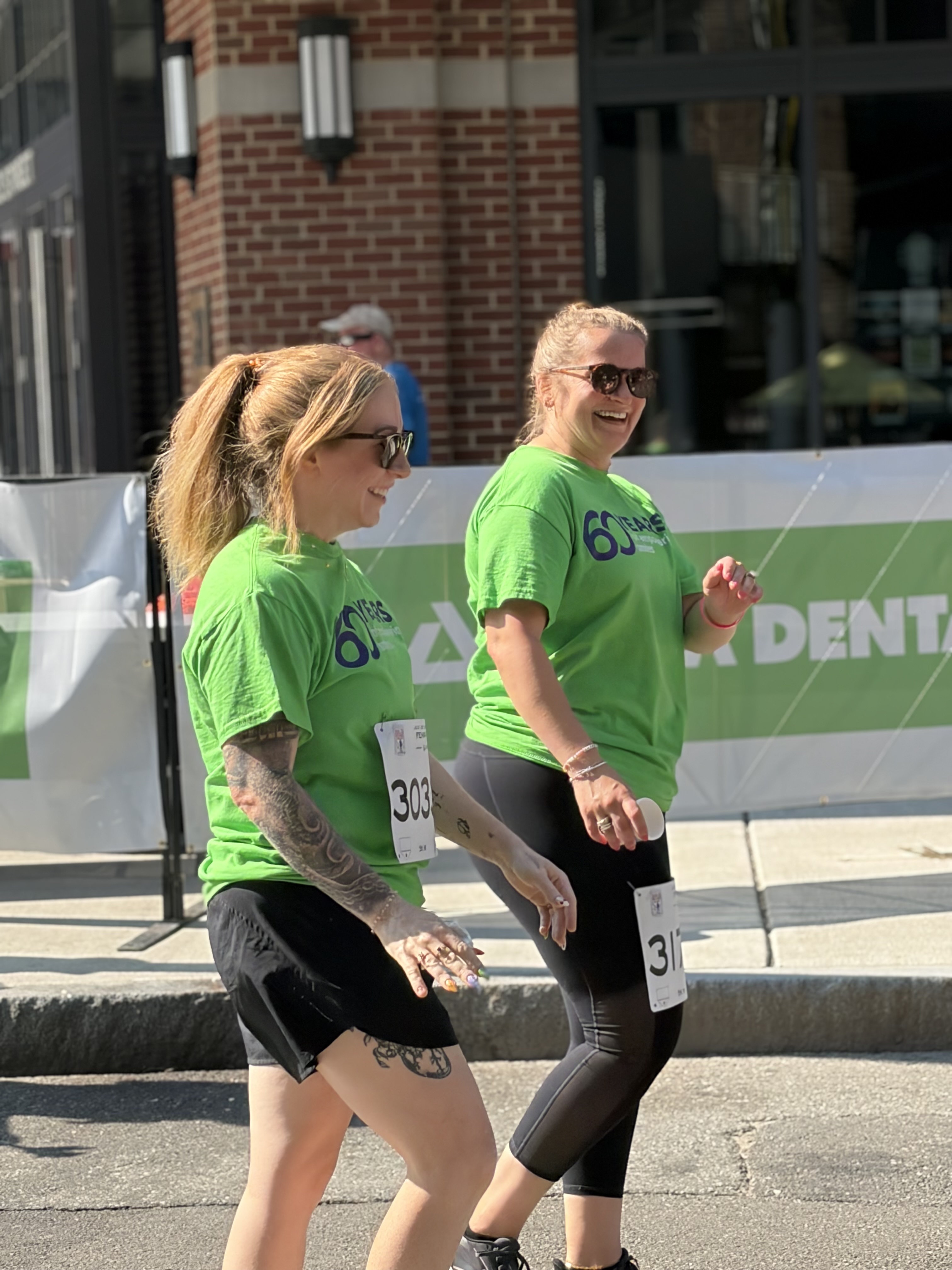 2 women wearing Delta Dental shirts walking the 5k race outside Fenway Park at Run to Home Base